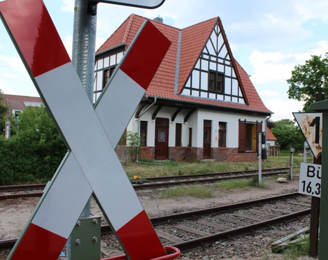 Sudweyher Bahnhof Ein altes Fachwerkgebäude mit Schrägdach am Bahngleis, markantes Kreuz in Vordergrund.