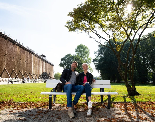 Herrlich zum Ausspannen: Der Kurpark in Bad Rothenfelde Ein Paar sitzt entspannt auf einer Parkbank vor einer Gradierwand an einem sonnigen Tag.