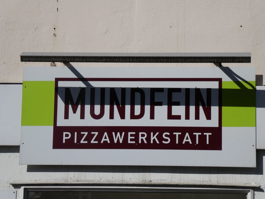 Mundfein Schild mit Aufschrift "Mundfein Pizzawerkstatt" auf hellen Hintergrund, mit modernem Design.