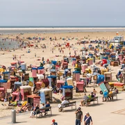 Strand mit bunten Strandkörben, Besuchern und Meerblick. Ein Sommertag voller Entspannung und Aktivität.Beach with colorful beach chairs, visitors and sea views. A summer day full of relaxation and activity.