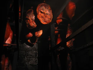 Schinken im Rauch Verschiedene Schinken hängen dicht beieinander im dunklen Raum, umgeben von mystischem Rauch.