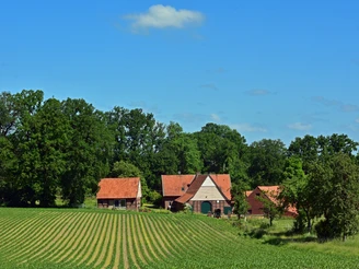 TERRA.track Kettelsberg  Drei Backsteinhäuser mit roten Dächern vor einem Feld und üppigem Baumbestand.