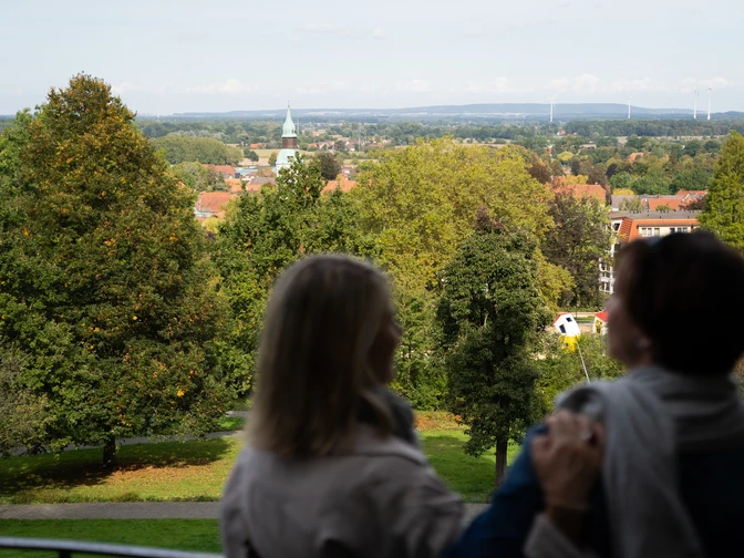 Blick von der Himmelsterrasse Zwei Personen genießen die Aussicht auf eine grüne Parklandschaft mit Kirchturm in der Ferne.