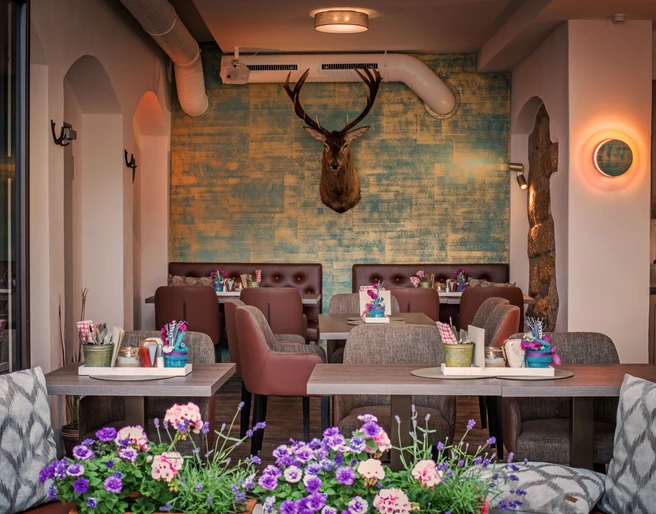 Restaurant Platzhirsch in Pirna Gemütliches Café mit braunen Sesseln, blumengeschmückten Tischen und einem Hirschkopf an der türkis-gelben Wand, im Vordergrund bunte Blumen.
