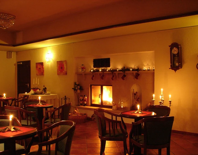 Gastraum Elbhotel Bad Schandau Gemütliches Café mit Kaminfeuer, Kerzen auf Tischen, warmem Licht und weihnachtlicher Dekoration, schafft eine einladende Atmosphäre.