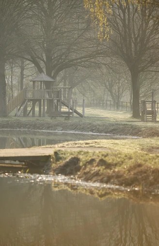 Ein ruhiger Teich in Etteln, umgeben von Bäumen und einem Holzsteg, im morgendlichen Nebel.