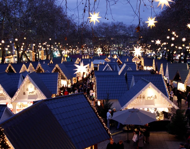 Market of Angels in Cologne Zauberhaft illuminierter Weihnachtsmarkt mit sternenförmigen Lichtern und Hütten unter freiem Himmel.Magically illuminated Christmas market with star-shaped lights and huts under the open sky.