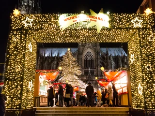 Christmas market at Cologne Cathedral Ein festlich beleuchtetes Eingangstor mit einem großen Weihnachtsbaum führt zum lebhaften Weihnachtsmarkt vor dem majestätischen Kölner Dom.A festively illuminated entrance gate with a large Christmas tree leads to the lively Christmas market in front of the majestic Cologne Cathedral.
