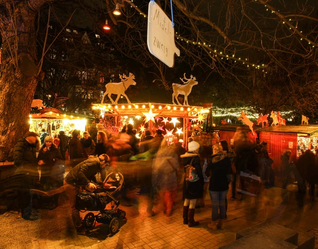 Stadtgarten Christmas market Ein belebter Weihnachtsmarkt im Stadtgarten Köln bei Nacht, mit leuchtenden Ständen und Menschen.A lively Christmas market in Cologne's Stadtgarten at night, with illuminated stalls and people.