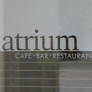 Atrium Schriftzug "Atrium Café Bar Restaurant" auf einer Glasoberfläche, dahinter verschwommene Gebäudestrukturen.
