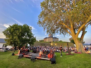 Veranstaltung Wilhelmstein Open-Air-Konzert auf einer grünen Wiese vor einer historischen Festung bei Sonnenuntergang.