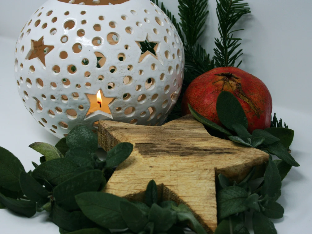 Handkunstwerke-zur-Weihnachtszeit-web.jpg Eine weiße Laterne mit Sternenmustern leuchtet sanft neben einem roten Granatapfel und grünen Zweigen.A white lantern with star patterns glows softly next to a red pomegranate and green branches.En hvid lanterne med stjernemønster lyser blødt op ved siden af et rødt granatæble og grønne grene.Een witte lantaarn met sterpatronen gloeit zachtjes naast een rode granaatappel en groene takken.