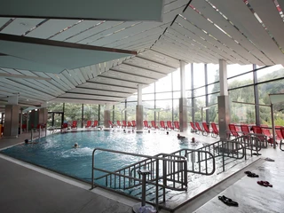 Aeskulap Therme in Schlangenbad Schwimmbecken in der Aeskulap-Therme in Schlangenbad. Hinter dem Schwimmbecken sind rote Liegestühle zu sehen. Sie sind in Richtung Fensterfront gedreht für einen schönen Ausblick.