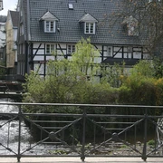 Velbert Langenberg Historische Fachwerkhäuser mit Graudächern säumen einen plätschernden Bach in Velbert Langenberg.