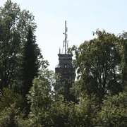Bismarckturm Velbert Ein steinerner Turm ragt zwischen dicht belaubten Bäumen hervor, umgeben von blauem Himmel.