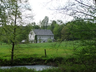 typischer Kotten im Ittertal, Brucherkotten Historischer Fachwerk-Kotten im Ittertal, umgeben von saftigem Grün und fließendem Bach im Vordergrund.