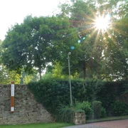 Sonnenstrahlen durchdringen Bäume neben einer gemauerten Wand mit einem Bibel-Pfahl in Gehrden.