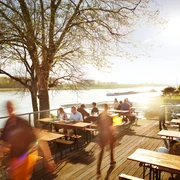 Haus Rheinblick Ott Eine belebte Terrasse am Flussufer des Rheins mit Menschen, die an Tischen speisen und genießen.