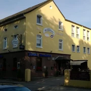 Gelbes Gebäude mit Gasthaus und Hotel in sonniger Umgebung, umgeben von Bäumen und Straße.