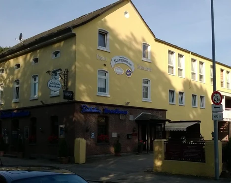 Gelbes Gebäude mit Gasthaus und Hotel in sonniger Umgebung, umgeben von Bäumen und Straße.