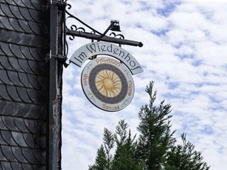 Außenschild vom Palazzo Wiedenhof in Haan Rundes Schild des Palazzo Wiedenhof in Haan mit dekorativem Sonnenmuster, umgeben von Bäumen.
