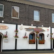 Taverna Symposion Das Bild zeigt ein traditionelles Restaurantgebäude mit weißen Wänden und dekorativen Blumen.