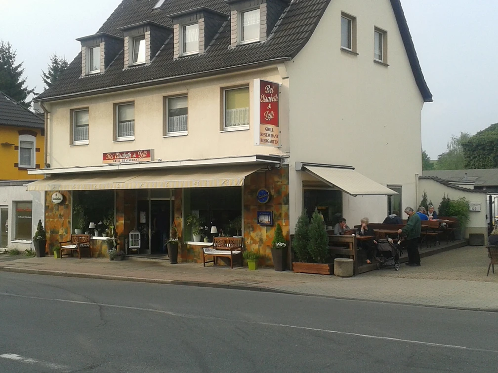 Ein zweistöckiges Gebäude neben einer Straße mit einem Café im Erdgeschoss und einer Außenterrasse.