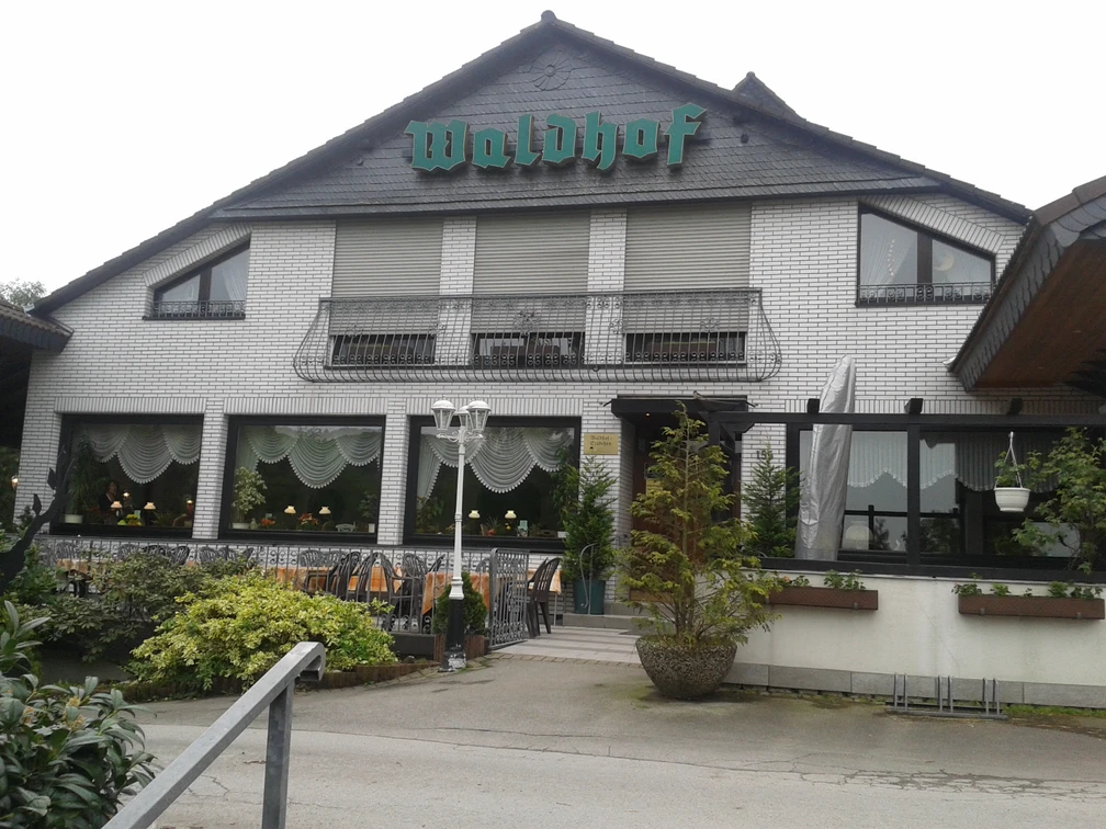 Café Restaurant Waldhof Weißes Backsteingebäude mit grünem Waldhof-Schild, Fenster mit Vorhängen und Laterne im Vordergrund.
