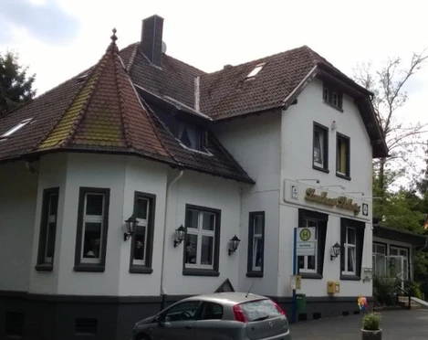 Landhaus Stolberg Ein zweistöckiges Landhaus mit Satteldach und Gaube, umgeben von Bäumen und mit parkenden Autos davor.
