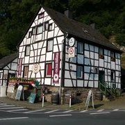 Fachwerkhaus mit Gaststätte, von Wald umgeben, bei strahlendem Sonnenschein an einer Straßenecke.