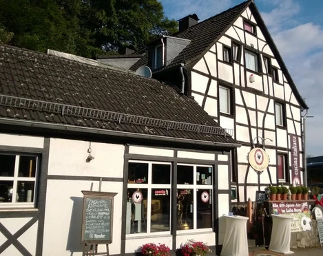 Fachwerkgebäude mit Blumen vor den Fenstern, in der Nähe ein Restaurant-Schild und Kerzendekoration.
