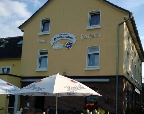 Ein gelbes Gebäude mit der Aufschrift "Knappmann Hotel Restaurant" und einem sonnigen Biergarten.