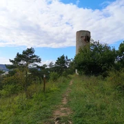 Ein steinerner Wachtturm auf einem bewaldeten Pfad, mit weitem Ausblick über die Hügel.