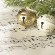 Weihnachtskonzert Goldene und silberne Glöckchen liegen auf Notenblättern, umgeben von Tannenzweigen.