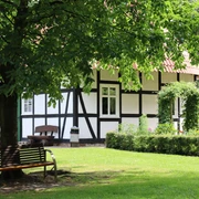 Fachwerkhaus im Kurpark Rothenuffeln, umgeben von Bäumen und einer gepflegten Grünfläche mit Bank.