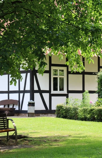 Fachwerkhaus im Kurpark Rothenuffeln, umgeben von Bäumen und einer gepflegten Grünfläche mit Bank.