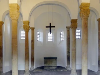 Rundbögen und Säulen umranden den Altarraum der Bartholomäuskapelle, betont durch schlichtes Kreuz.