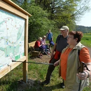 Infotafel im Ellerbachtal Wanderer studieren eine Karte des Paderborner Karstrundweges an einer Holzinfotafel im Ellerbachtal.