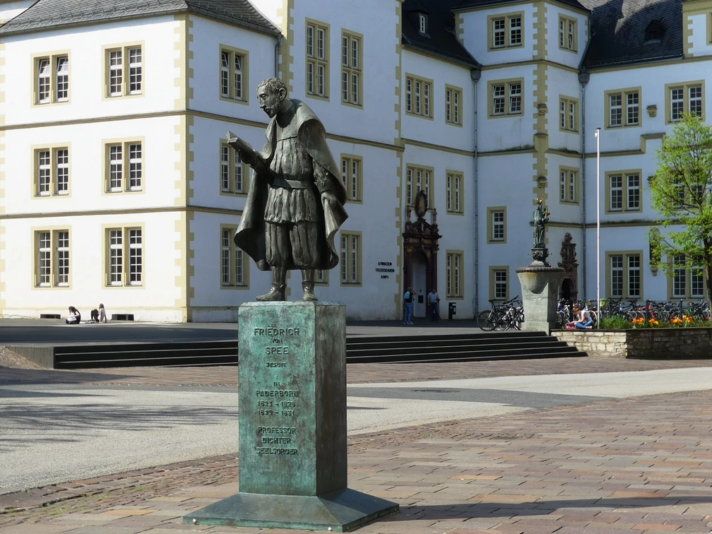 Bronzestatue Friedrich Spees, im Vordergrund eines historischen Schulgebäudes, mit Stufen.