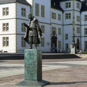 Bronzestatue Friedrich Spees, im Vordergrund eines historischen Schulgebäudes, mit Stufen.