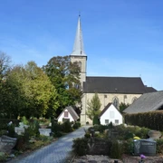 Pfarrkirche St. Margaretha in Dahl mit gravierten Grabsteinen, umgeben von Bäumen bei sonnigem Himmel.