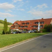 Außenansicht Ein traditionelles Gebäude mit rotem Satteldach vor einer grünen Wiesenlandschaft und blauen Himmel.