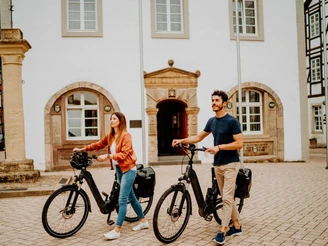 Marktplatz Brakel Zwei Personen schieben ihre E-Bikes über den gepflasterten Marktplatz vor historischen Gebäuden.
