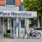 Tourist-Info Rheda-Wiedenbrück Ein Eingang zur Tourist-Information Flora Westfalica mit zwei Fahrrädern vor modernen Gebäuden.
