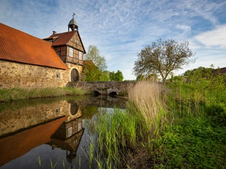 Gut Stockhausen Historisches Fachwerkgebäude an einem Wassergraben mit Steinbrücke, von Vegetation umgeben.