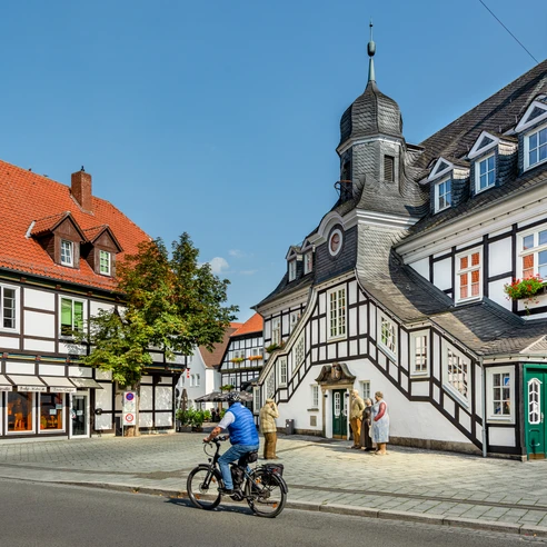 Rietberg-RathausRadfahrer-prowiGT-Wallenfang.jpg Historische Fachwerkhäuser mit markantem Türmchen und Radfahrer bei sonnigem Wetter in Bad Essen.