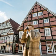 Eine Holzfigur in traditioneller Kleidung fotografiert Fachwerkhäuser in einer historischen deutschen Stadt.