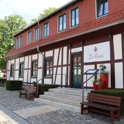 Die Rentei Fachwerkgebäude mit roten Akzenten, Treppenstufen führen zum Eingang, von Bänken flankiert.