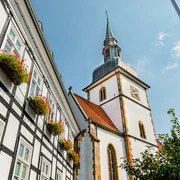 Historisches Fachwerkgebäude neben der St. Ursula-Kirche mit blühenden Pflanzen im Vordergrund.