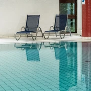 Symbolbild: Schwimmbad Innenpool mit zwei blauen Liegestühlen und großen Fenstern, die natürliches Licht hereinlassen.
